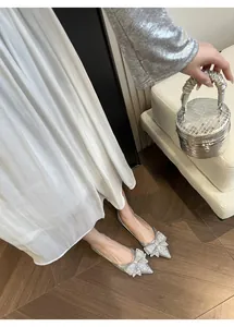 Eleganti ballerine a punta argento con fiocco di strass, abbinate a un abito bianco.