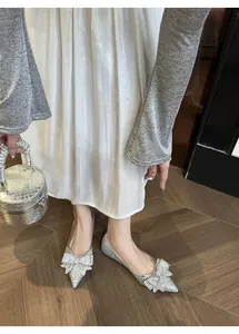 Dettaglio di ballerine a punta argento con decorazioni a fiocco in strass luccicanti.