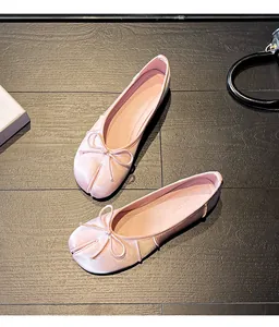 Detail of pink split-toe tabi ballet flats featuring a bow on dark wood flooring.