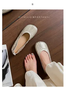 Primo piano delle ballerine a pieghe stile Tabi beige su pavimento in legno