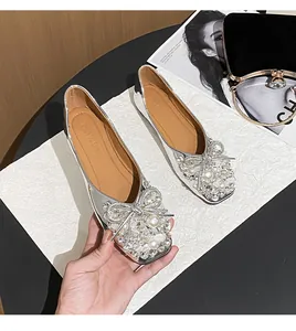Detailed view of elegant silver flat shoes featuring a rhinestone bow and pearl accents.