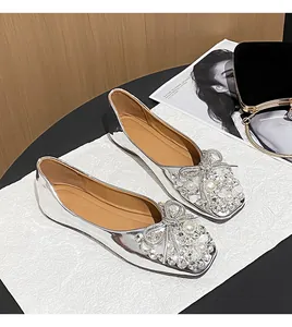 Close-up of silver flat shoes featuring ornate pearl and rhinestone bow decorations.