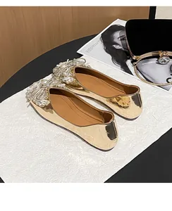 Close-up view of gold metallic flat shoes with intricate rhinestone and pearl bow details