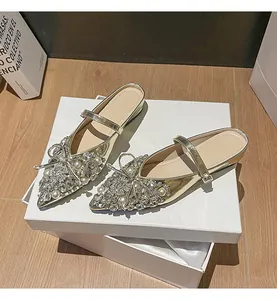 Detailansicht der goldenen flachen Pantoletten mit Strass- und Perlen-Schleife