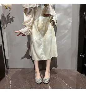 Detailaufnahme eleganter flacher Schuhe mit Strassschleife und einem Satinrock in Champagner.