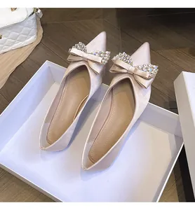 Dettaglio delle ballerine a punta in raso champagne con fiocco di strass scintillanti.