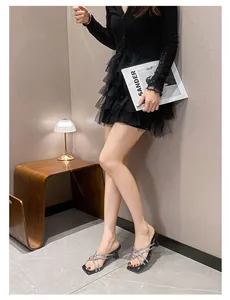 Elegant black high-heel sandals with rhinestone cross straps shown on a model in a room
