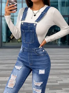 Close-up of women's blue slim-fit stretch denim overalls with distressed ripped details.