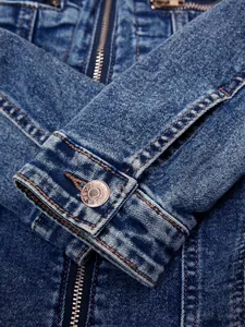 Close-up detail of a blue denim jacket sleeve showing the metal button and zipper.