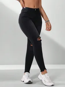 Detailweergave van een zwarte stretch skinny jeans voor dames met gescheurde knieën en zomen.