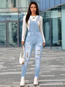 Full-body view of slim fit distressed denim overalls in a modern urban street setting.