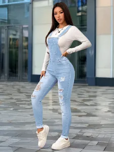 Full body detail view of women's slim fit distressed light blue denim overalls set