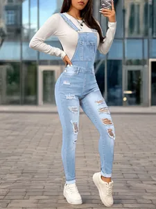 Full-length outdoor view of women's slim-fit light blue ripped denim overalls with pocket