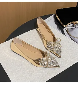Dettaglio di eleganti ballerine da sposa dorate a punta con fiocchi di strass scintillanti.
