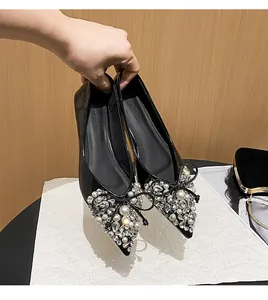 Eleganti ballerine nere a punta con perle, strass e fiocco decorativo, tenute in mano.