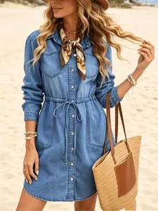 Chic long-sleeve denim mini dress with drawstring waist on a sunny beach setting.