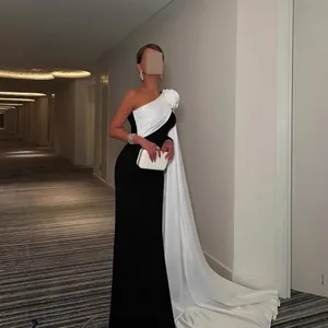 Elegante tweekleurige avondjurk met groot roosdetail en een lange vloerlange cape.
