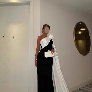 Elegante zwart-witte avondjurk met één schouder, grote bloem en een lange vloeiende cape