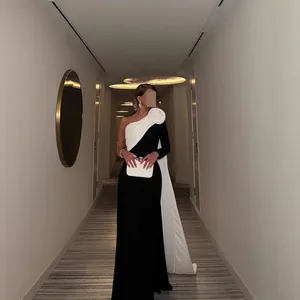 Elegante zwart-witte avondjurk met één schouder, groot bloemdetail en vloerlange cape