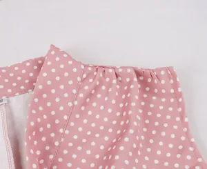 Gros plan sur les plis de l'épaule d'une robe rétro rose à pois blancs sans manches