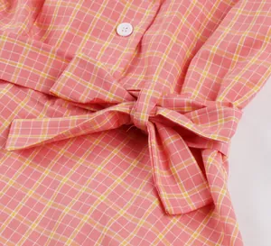 Detalle de un vestido de cuadros rosa con un lazo en la cintura y botón blanco.