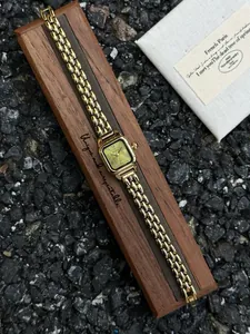 Vintage gold square women's watch with green dial and Roman numerals on a wooden box