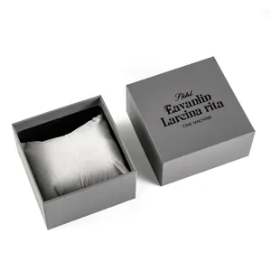 Close-up view of a textured grey square watch gift box with a light grey cushion inside