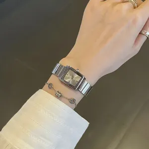 Elegante reloj cuadrado plateado con esfera minimalista usado en la muñeca con joyas.