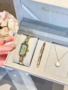 Gros plan sur une montre dorée, un jonc et un collier dans un coffret cadeau gris
