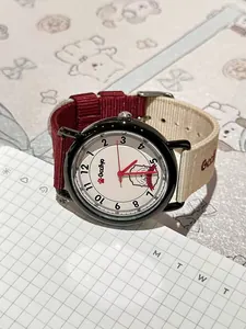Detailed macro view of a student quartz watch featuring a red and cream striped nylon strap.