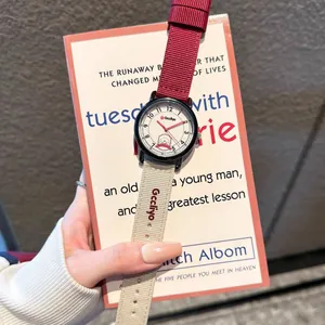 Minimalist student quartz watch with red and beige fabric strap against a book background.
