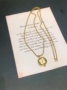 Close-up of vintage square gold watch pendant on a decorative parchment background.