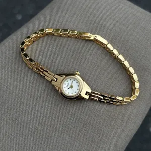 Montre à quartz vintage dorée pour femme avec bracelet à maillons sur fond gris
