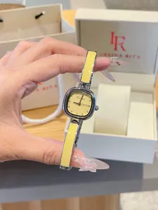 Élégante montre bracelet carrée jaune tenue à la main avec boîte cadeau en arrière-plan.