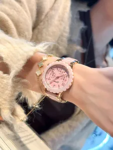Nahaufnahme einer rosa Luxusuhr und eines goldenen Kleeblatt-Armbands am Handgelenk.