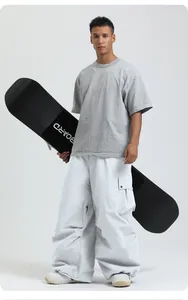 Loose white waterproof ski pants for winter sports shown by a model with a snowboard