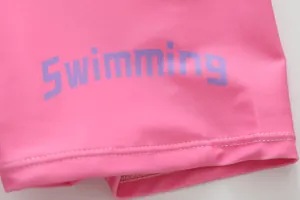 Macro detail of pink children's swimsuit fabric featuring a purple Swimming print