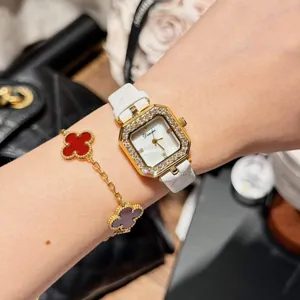 Close-up of elegant Dimini square gold watch with diamond bezel and white leather strap
