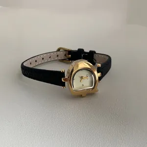Detalle de un reloj vintage de mujer dorado en forma de G con correa de cuero negro