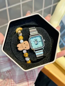 Primer plano de un lindo reloj de cuarzo cuadrado con esfera de pingüino y set de pulseras.