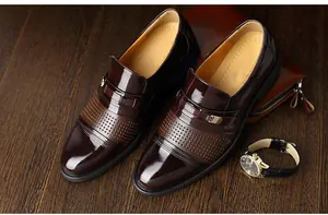 Close-up detail of men's glossy burgundy leather loafers with decorative perforations