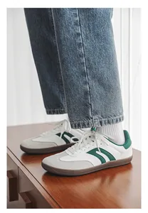Detailed side view of white and green wide-toe sneakers on a wooden surface.