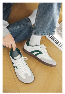 Lifestyle detail of white wide-toe sneakers with green accents and gum soles.