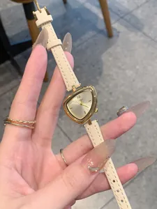 Primo piano dettagliato di un orologio dorato triangolare con cinturino in pelle crema