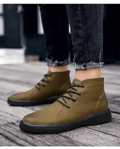 Detail shot of men's olive green leather boots with black laces on wooden floor.
