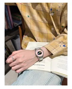 Gros plan d'une montre chat mignonne au poignet avec chemise jaune et livre ouvert.