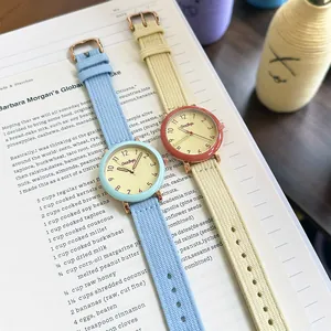 Two minimalist women's quartz watches with pastel fabric straps and simple numeric dials.