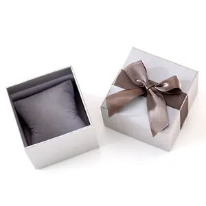 Detalle de caja de regalo plateada para reloj con lazo marrón y cojín.