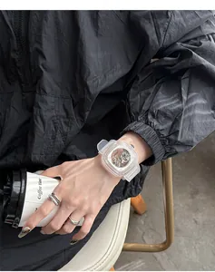 Fashionable transparent square mechanical watch with a white silicone strap worn on wrist