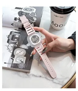 Close-up of pink mechanical watch with transparent square case held over a lifestyle magazine